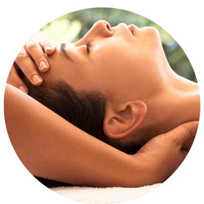 Une personne couchée sur une table de massage reçoit un massage crânien avec les mains d’un thérapeute qui lui applique une pression sur le cuir chevelu, le front et la nuque.