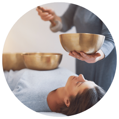 Une personne allongée sur une table de soin reçoit un massage sonore avec des bols tibétains et des diapasons thérapeutiques